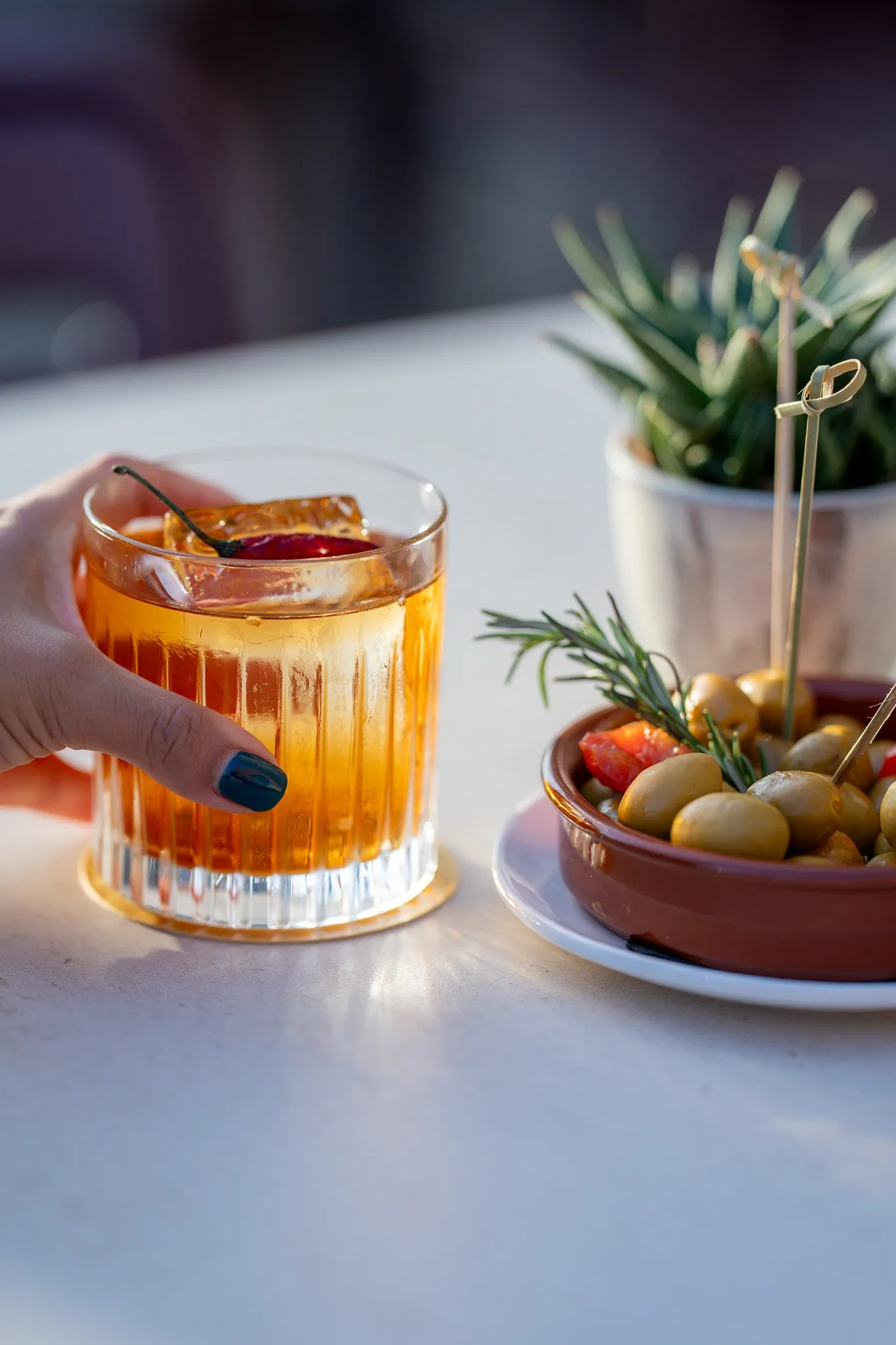 Cóctel old fashioned y aceitunas sobre una mesa de mármol